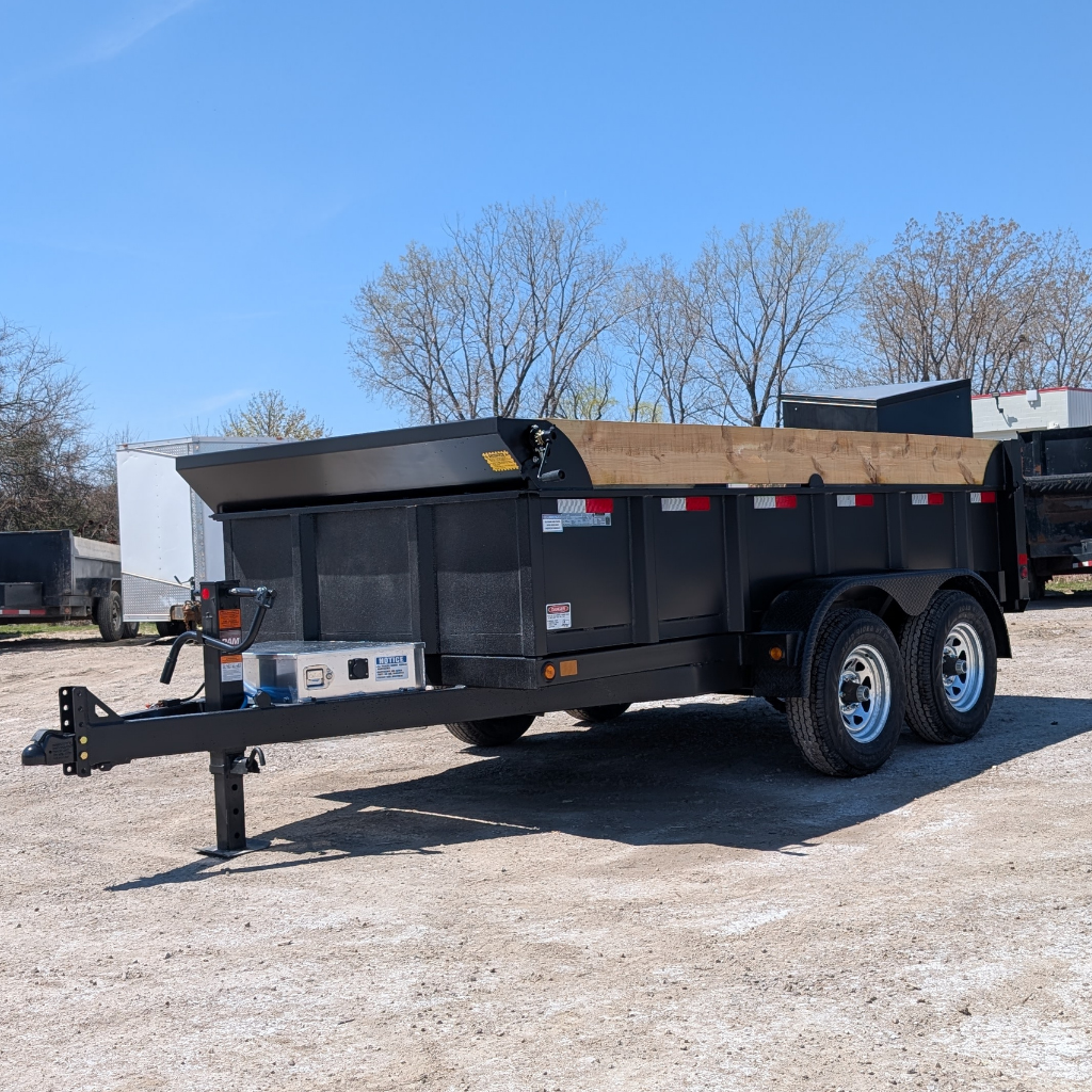 A 2025 CANADA TRAILER 6X12 DUMP 10,000 GVWR with wooden side extensions is parked on a gravel lot, surrounded by trees and other trailers under a clear sky.