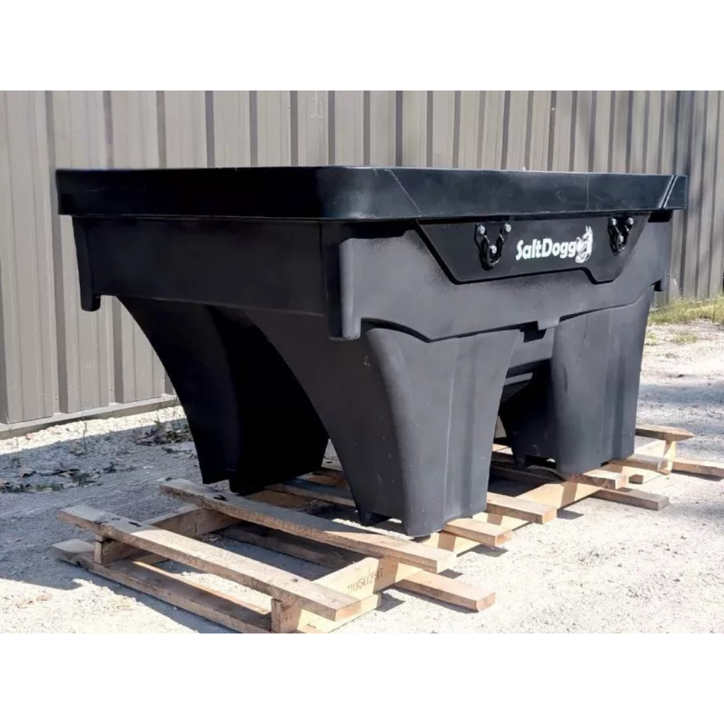 A SALT DOGG 1500 1.5-YARD SALTER in black rests on a wooden pallet outside, positioned in front of a building with metal siding.