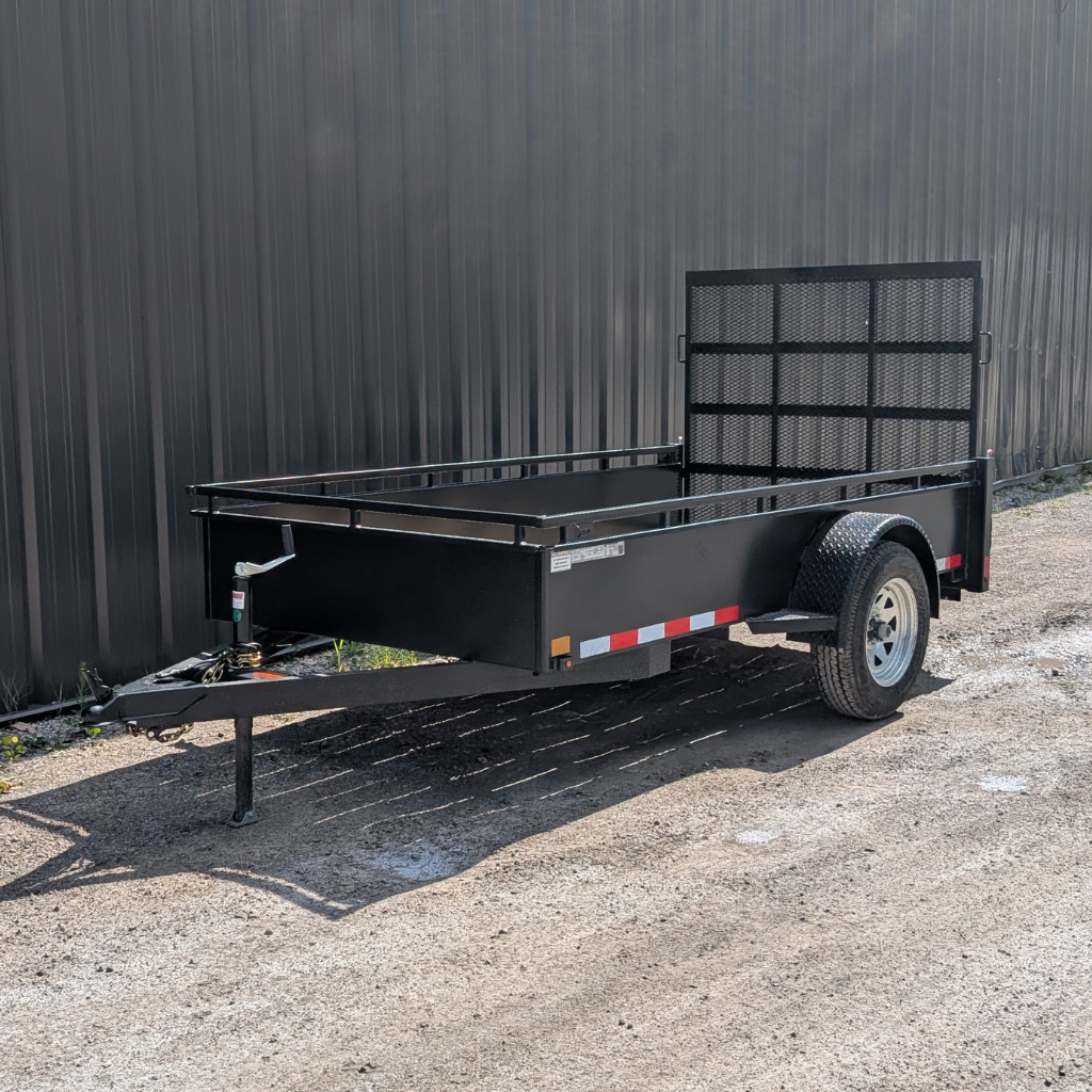 A 2026 CANADA TRAILER 5X10 Steel Side Utility Trailer (2990 GVWR) with single axle and ramp gate is parked on gravel beside a metal-sided building.
