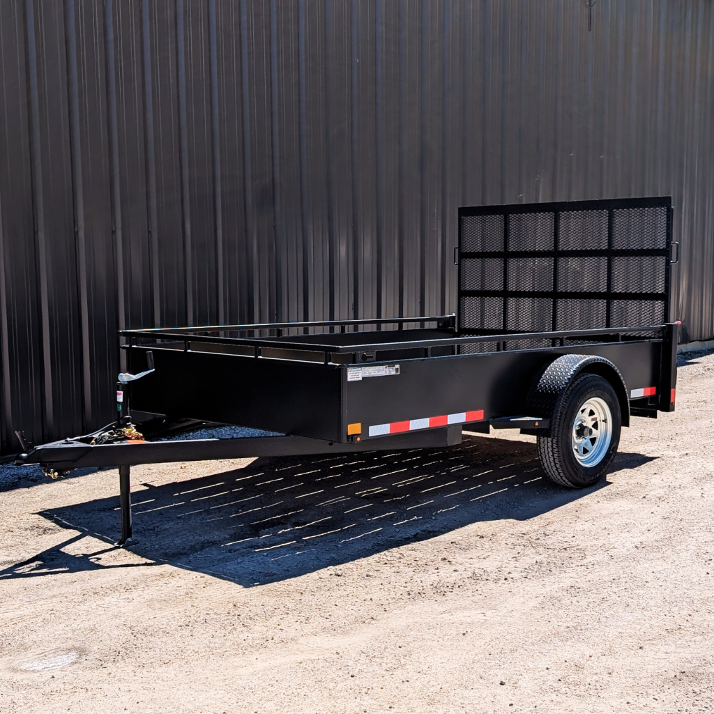 A 2026 CANADA TRAILER 6X10 steel side utility trailer (2990 GVWR) with a metal mesh ramp is parked on gravel in front of a corrugated metal wall.