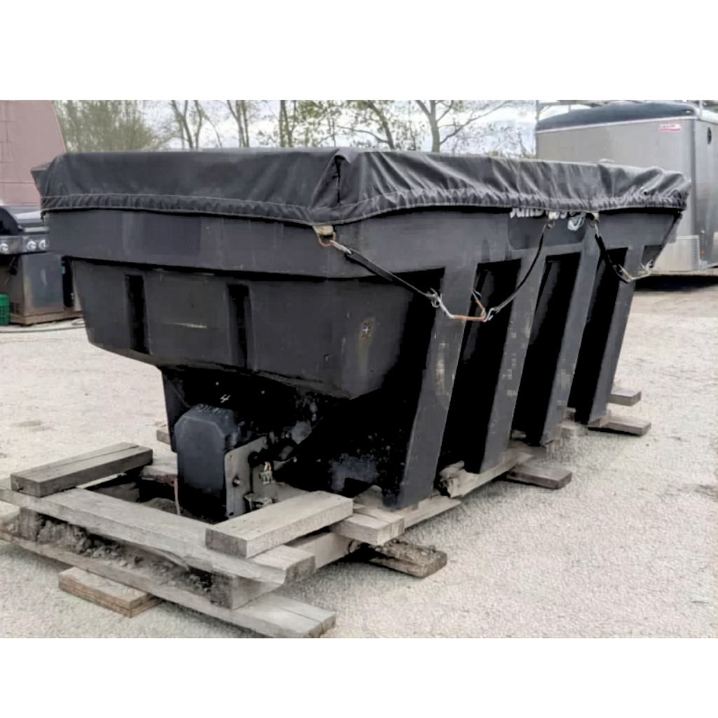 A Salt Dogg 2000 2-yard salter, black and industrial, is covered with a tarp and set outdoors on wooden pallets.