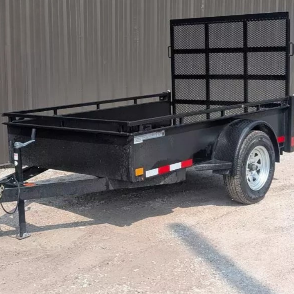 A 2025 CANADA TRAILER 5x8 steel side utility trailer with a mesh ramp gate and single axle is parked on gravel near a metal building.
