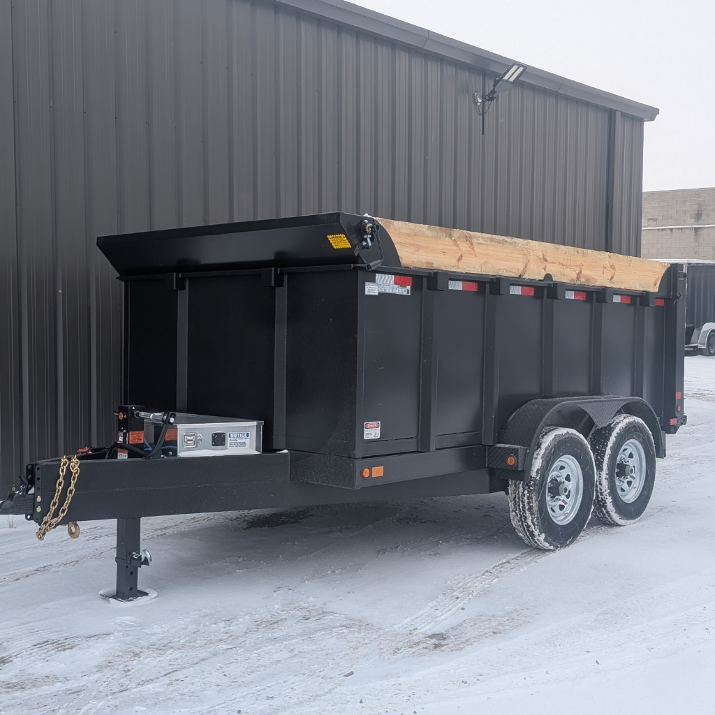 A 2026 CANADA TRAILER 83X12 DUMP HIGH SIDE 48" 14000 GVWR is parked on a snowy surface next to a brown metal building.