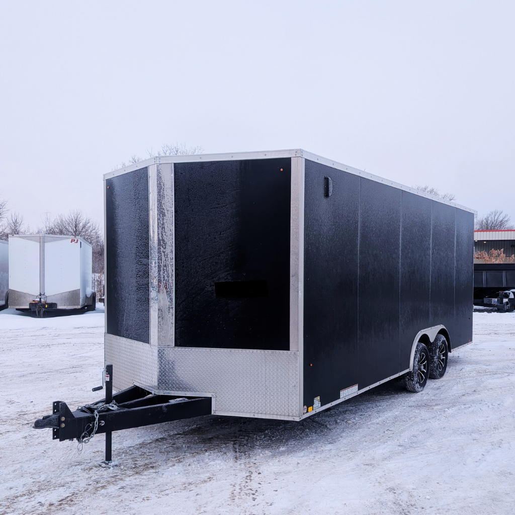 A 2026 PACE 85X20 DLX OUTBACK FLAT TOP trailer in black with a ramp door and 12" extra height is parked on a snowy lot, alongside other trailers.