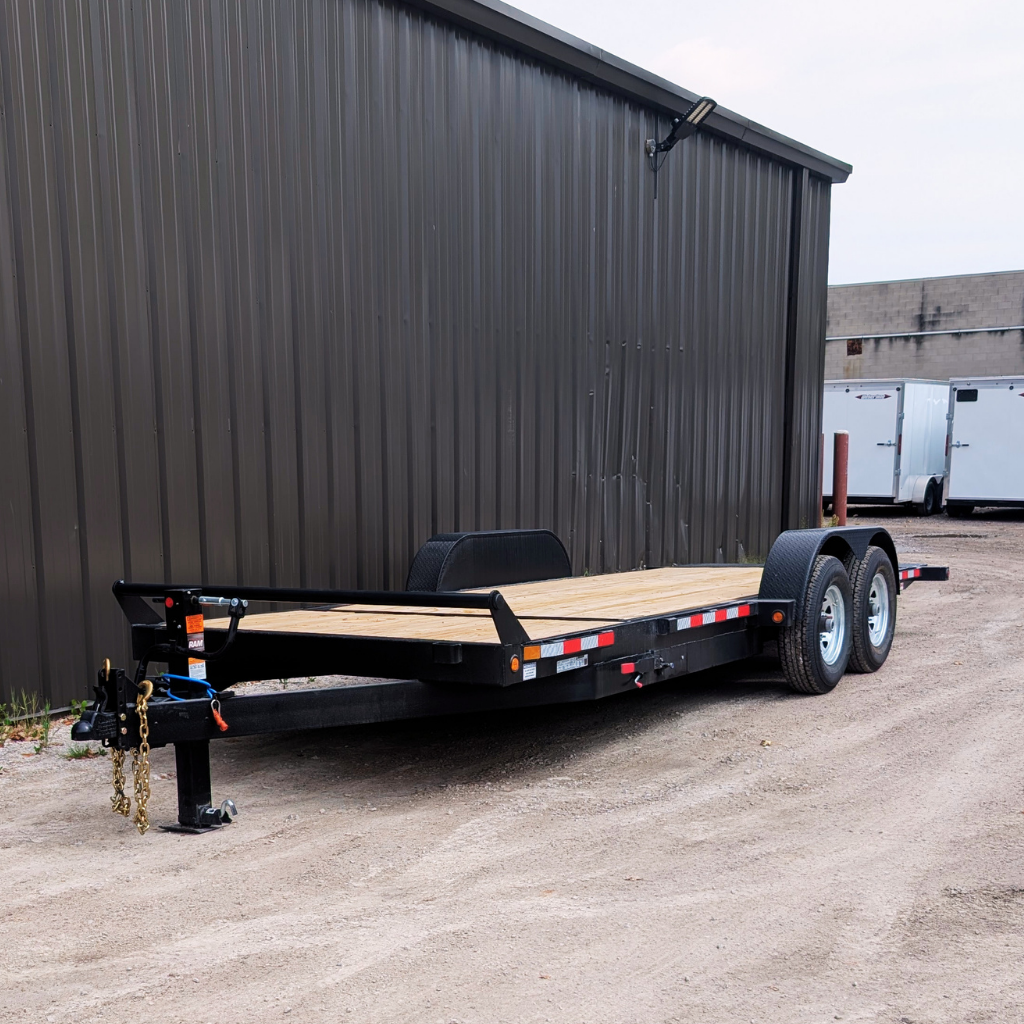 A 2026 CANADA TRAILER 7X21 GRAVITY TILT 14,000 GVWR flatbed utility trailer is parked on a gravel lot next to a large metal building.