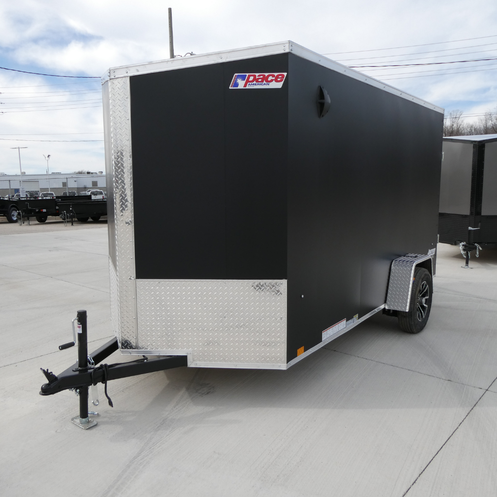 A 2023 PACE JV6X12SI2SE Journey SE flat top matte black enclosed cargo trailer with 24" sloped nose, 6" extra height, ramp door, and single axle is parked on a concrete lot.