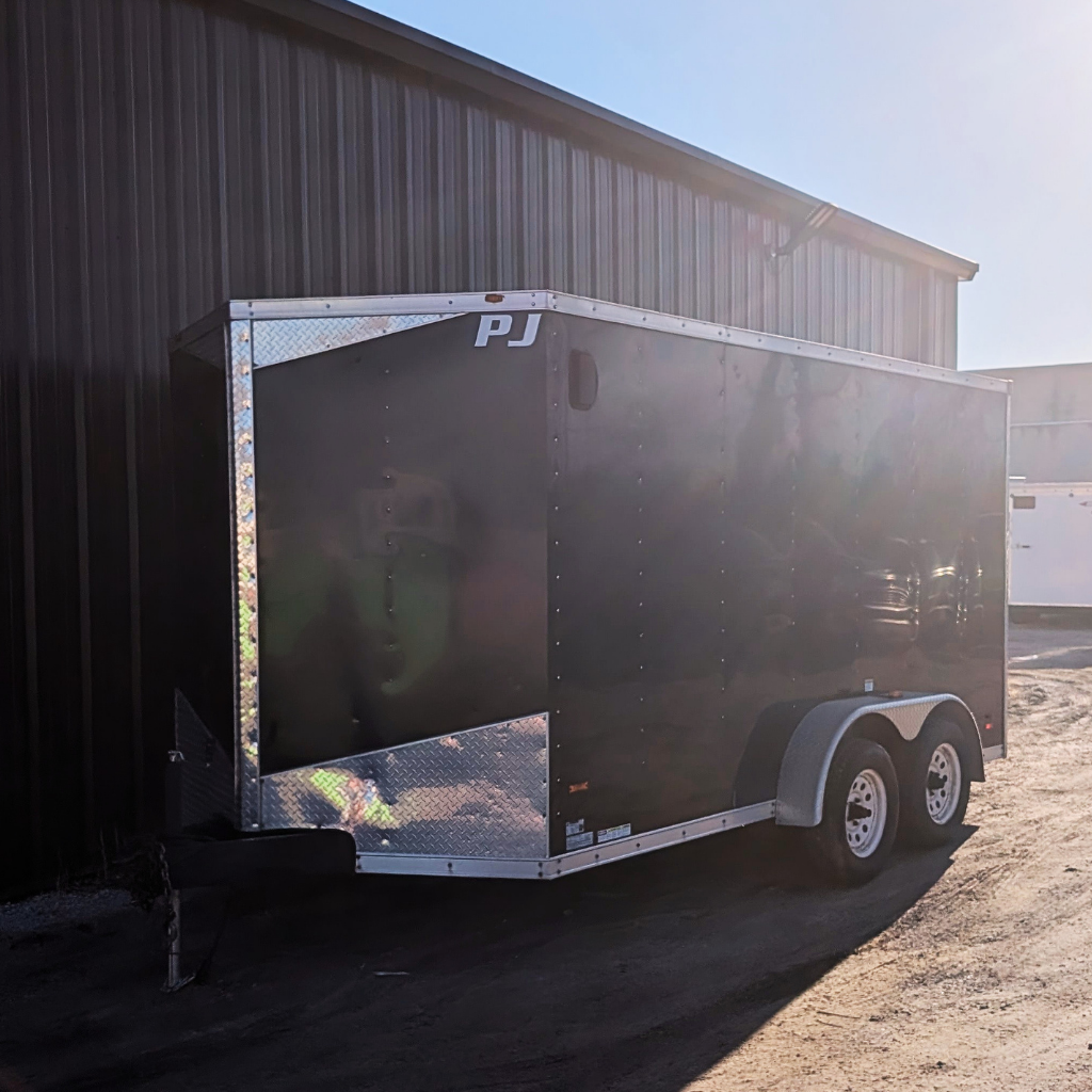 A used 2015 MTI 7x14 enclosed ramp door trailer in black is parked beside a metal building in sunlight.